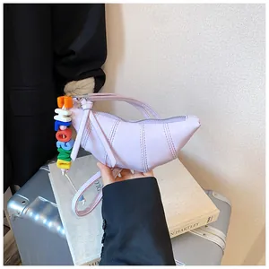Detail der fliederfarbenen Croissant-Tasche mit Falten-Effekt und buntem Buchstabenanhänger