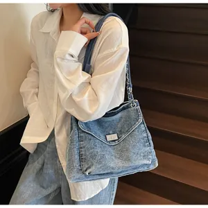 Détail d'un sac messager en jean bleu avec chaîne argentée porté avec une chemise blanche