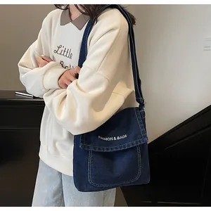 Détail du sac à bandoulière en denim bleu foncé avec broderie blanche et fermeture à rabat