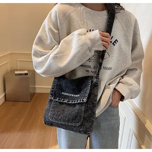 Détail du sac bandoulière en denim foncé montrant la texture et le logo sur le rabat