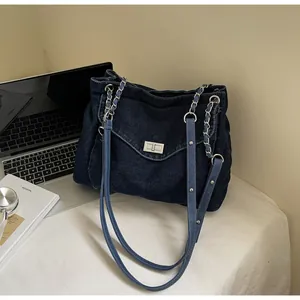 Close-up of a blue denim tote bag with a silver metal twist-lock and chain strap