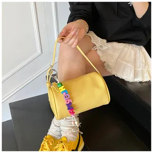 Detail view of yellow cylinder shoulder bag featuring colorful letter beaded charm and lychee texture