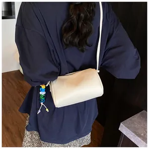 Rear view of a cream cylinder crossbody bag featuring colorful 'JUNE' letter beads