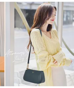Detail of teal leather crossbody bag with V-shaped gold logo on a yellow knit cardigan