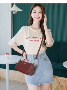 Fashionable burgundy leather crossbody bag with golden deer logo on casual chic outfit