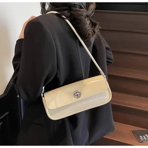 Beigefarbene Lackleder-Baguette-Tasche mit silbernem Drehverschluss am Model getragen