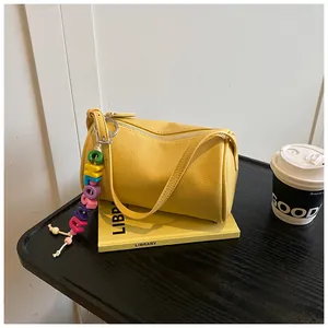 Detail of a bright yellow Boston style shoulder bag with leather texture and bead pendant