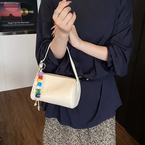 Chic beige textured leather cylinder shoulder bag with a colorful alphabet bead charm