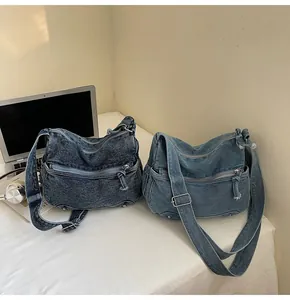 Dettaglio delle borse a tracolla in denim lavato con pratiche tasche con cerniera multipla