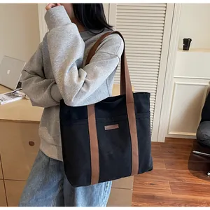 Détail du sac cabas en toile noire avec lanières marron et écusson en cuir style lifestyle