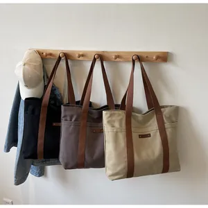 Vue détaillée de sacs fourre-tout en toile noir, marron et beige suspendus sur des crochets