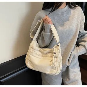 Detail of off-white canvas crossbody bag showing multiple functional zipper pockets