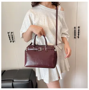 Petit sac carré rouge foncé brillant avec boucle argentée posé sur un siège en cuir