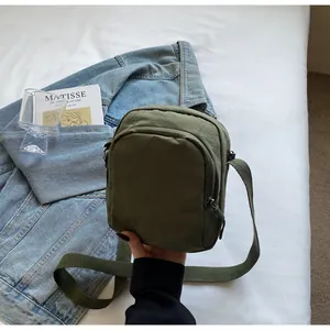 Olivgrüne wasserdichte Nylon-Umhängetasche über Jeansjacke und Kunstbuch gehalten