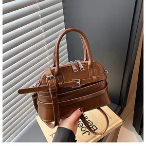 Detail of dark brown leather handbag with silver buckles and dual zipper closure on books
