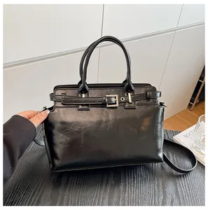 Détail d'un sac à main noir en similicuir brillant avec boucle argentée et bandoulière