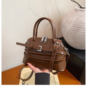 Close-up of brown leather shell bag with decorative buckle and silver zipper