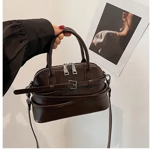 Detail of a dark brown glossy shell-shaped handbag with silver hardware and smooth texture