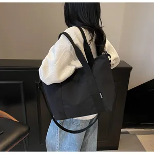 Détail d'un grand sac cabas noir avec bandoulière réglable présenté sur un mannequin
