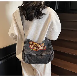Close-up of grey denim messenger bag with embroidered stars and vintage style text