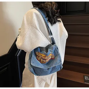 Detail of adjustable strap and denim embroidery on blue crossbody tote bag