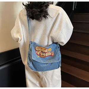Detail of blue denim crossbody bag with colorful embroidery on a wide shoulder strap