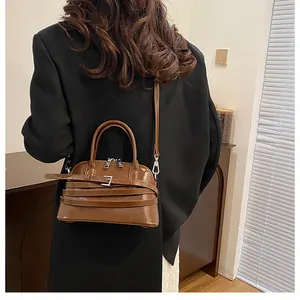 Rear view of brown glossy leather crossbody bag with silver hardware on a dark coat