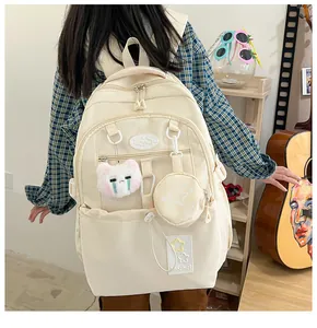 Détail d'un sac à dos crème avec pochette ronde et peluche de chat blanc sur un mannequin