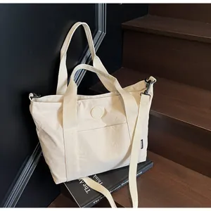 Détail du sac cabas en toile crème avec bandoulière réglable sur un escalier en bois