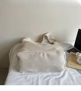 Close-up of beige woven tote bag with Intrecciato pattern next to a laptop
