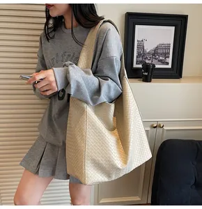 Detail view of woven leather texture on a beige oversized tote bag with wide shoulder strap