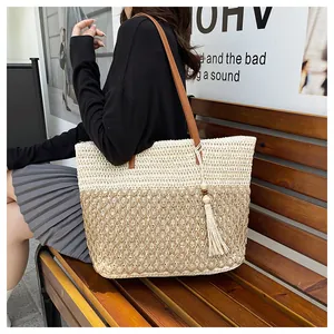 Detail of a large woven tote bag with contrast stitching and beige tassel charm decoration