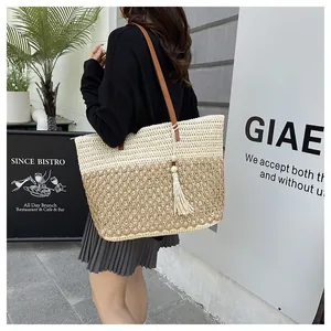 Detail of a large woven tote bag with brown leather straps and tassel on shoulder