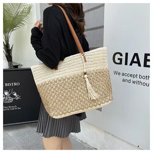 Detail of a large woven tote bag featuring color-block design and chic tassel pendant