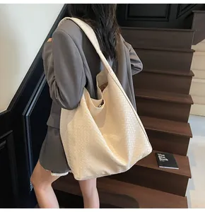 On-shoulder view of large cream woven leather bucket bag with wide strap for daily commute
