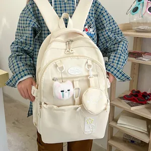 Gros plan du sac à dos beige avec compartiments multiples et breloque chat en peluche