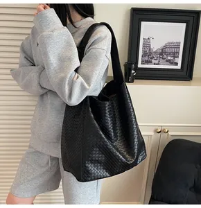 Close-up of black woven leather bucket tote bag with wide shoulder strap on a model