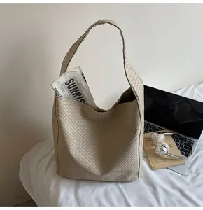 Close-up of beige woven texture hobo bag with wide shoulder strap on bed