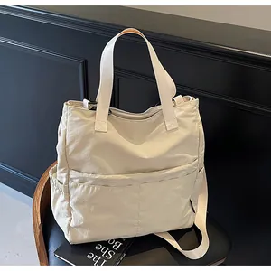 Detail van een crème nylon draagtas met voorzakken geplaatst op een zwarte leren stoel