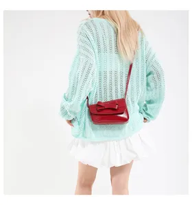 Detail of red crossbody bag with bow accent worn over a light green knit sweater