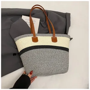 Detail of a three-tone woven straw tote bag with brown leather handles on a grey blazer