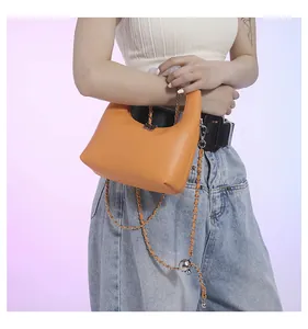 Sac à main trapèze en cuir orange avec chaîne argentée porté par un mannequin
