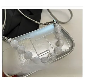 Dettaglio della borsa squadrata argento con texture metallica e catena decorativa di perle