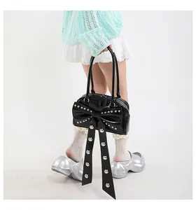 Détail du sac à main noir brillant avec grand nœud et rivets argentés de style Y2K