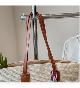 Detail of woven straw tote bag featuring brown leather handles with contrast stitching