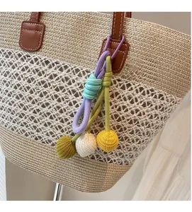 Detail of colorful woven rope pendant with spherical tassels on a beige straw tote bag