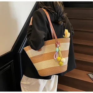 Detail of striped woven straw tote bag with colorful pom-poms and leather shoulder strap