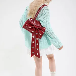 Sac à bandoulière rouge foncé avec nœud et rivets argentés porté par un mannequin