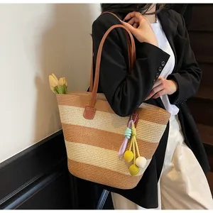 Detail of striped woven tote bag featuring leather straps and colorful pompom charm