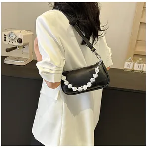 Dettaglio di una borsa sottobraccio nera con grandi perle bianche decorative sulla catena